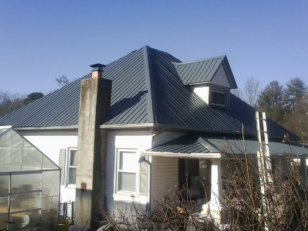 Dark blue standing seam metal roof on a white farmhouse with dormer — Slate & Tile Roof Repair by Roofing Brothers in Malone
