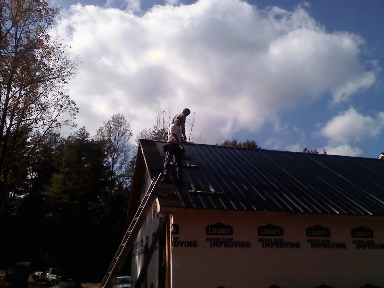 Roofer fastening dark metal panels high against a cloudy sky, from a Roof Inspection job in Malone