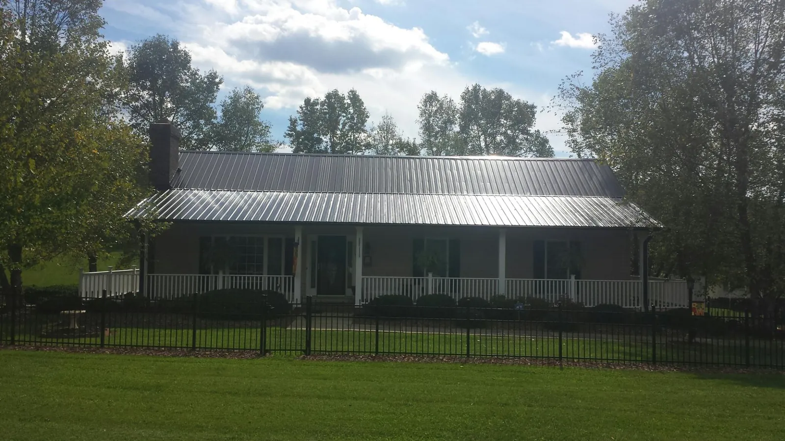 Gray metal roof on a brick ranch with a full width front porch — Gutter Guard Installation work by our crew in Malone