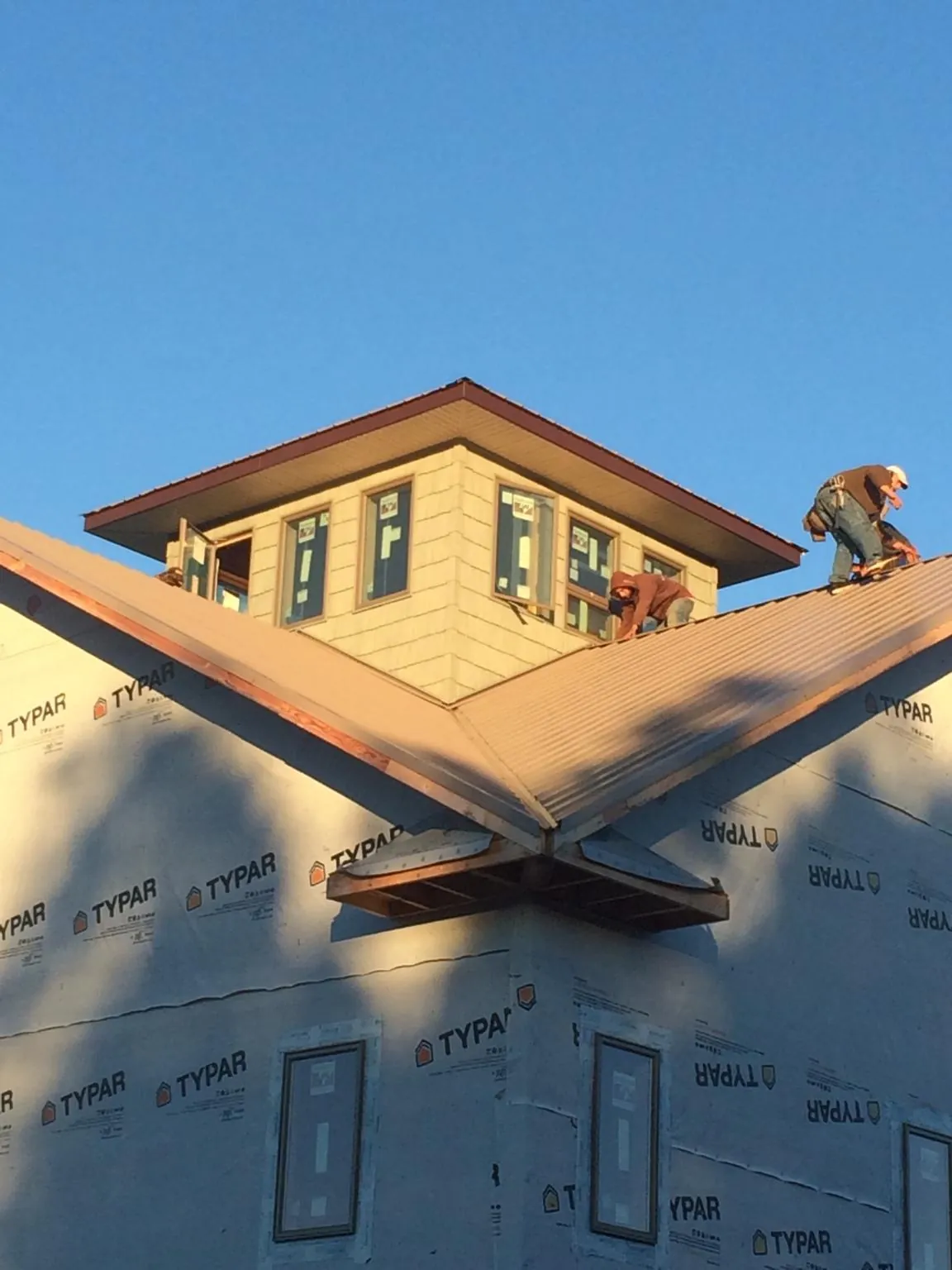 Roofers working around a rooftop cupola on a new metal roof at sunset — Roof Waterproofing in Malone by Roofing Brothers